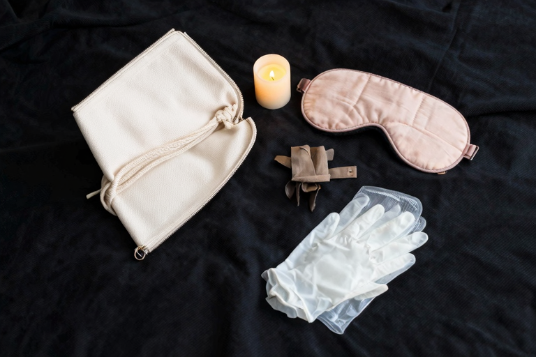 暗い部屋に置かれた低温キャンドル、スカーフ、ファー付き手錠——ポーチに収まるミニマムSMツールのイメージ